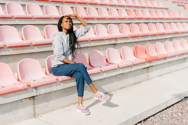 Joven mujer afroamericana mirando a la distancia frente a los bancos del estadio moderno — Foto de Stock