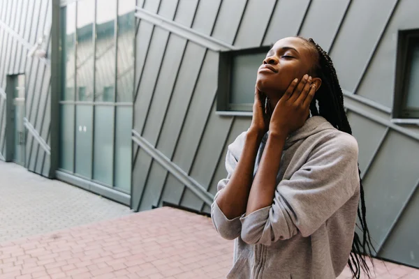 Levensstijl en mensen concept - glimlachen Afrikaanse Amerikaanse jonge vrouw of tienermeisje in koptelefoon luisteren naar muziek sluiten oren met haar handen buitenshuis — Stockfoto