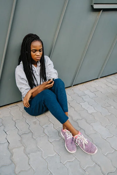 Portrett av en vakker, trist, tenksom ung kvinne med langt hår i hodetelefoner som sitter på fortauet – stockfoto