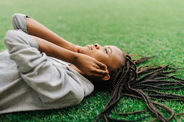 Menina americana africana jovem pensativo deitado na grama ouvindo música com fones de ouvido — Fotografia de Stock