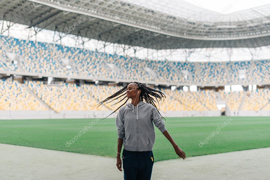 Beautiful african american female in sportswear dancing swinging her braided hair alone at empty stadium