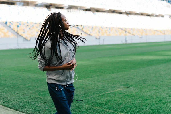 Metade do corpo retrato de uma mulher afro-americana de capuz cinza correndo ao ar livre no estádio vazio — Fotografia de Stock