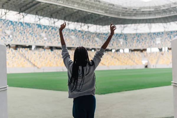 Indietro di donna afro-americana in piedi tra lo stadio vuoto a festeggiare, le braccia alzate a pugni l'aria con le mani — Foto Stock