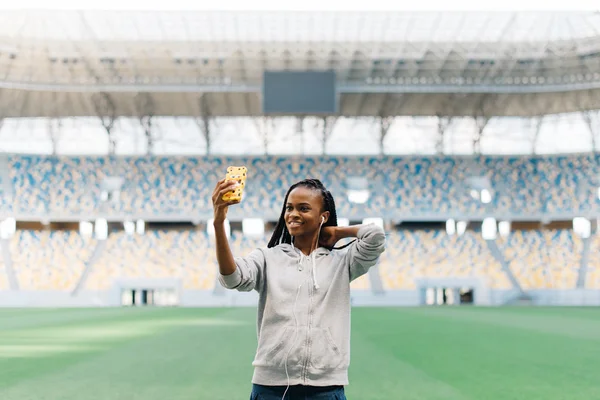 Retrato de uma bela mulher esportiva com seu cabelo trançado fazendo foto selfie no smartphone no estádio vazio — Fotografia de Stock