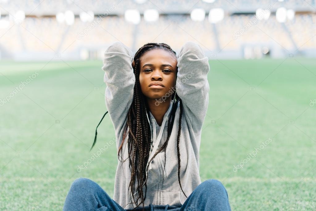 Unhappy and frustrated african american woman sitting with her hands behind head on the green grass