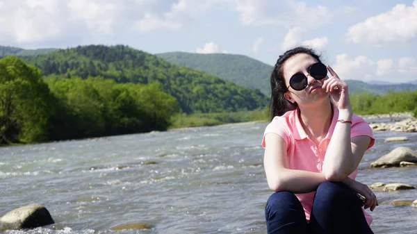 Retrato de sorrir bela jovem sentada na pedra no rio da montanha — Fotografia de Stock