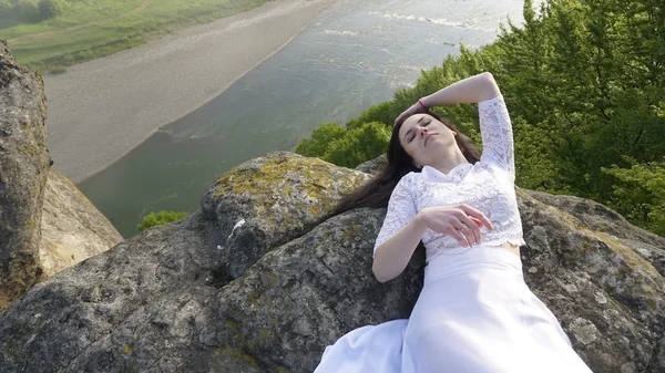 Portret zadumany Panna Młoda w sukni ślubnej biały leżącą na skałach tylko w pobliżu rzeki — Zdjęcie stockowe