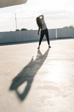 Günbatımında dans eden genç Afrikalı Amerikalı kadın kulaklıklarıyla müzik dinlerken, arka plan olarak şehir manzarası