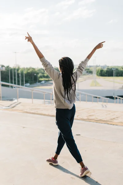 Silhouette di felice ragazza afro-americana alzato le mani al sole, in piedi su sfondo urbano — Foto Stock