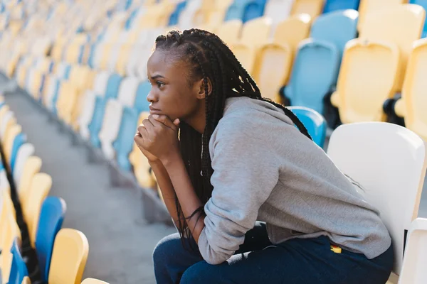 Vue latérale de la femme afro-américaine assise la tête sur les mains et se sentant déçue contre les rangées de stade — Photo