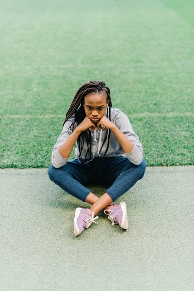 Mujer joven afroamericana aburrida sentada en el estadio vacío con la barbilla apoyada en las manos y una expresión sombría —  Fotos de Stock
