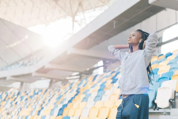 Jistá africká americká mladá žena stojící v řadách prázdných sedadel na stadionu s rukama za hlavou — Stock fotografie
