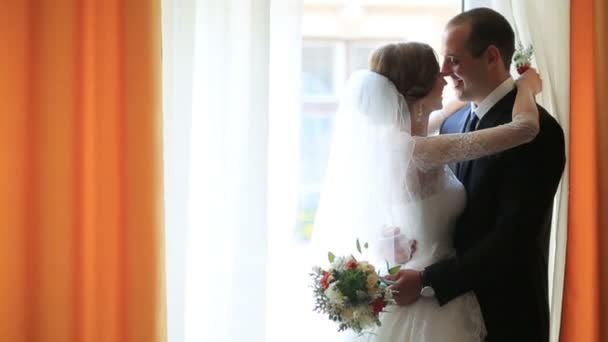 Gyönyörű fiatal pár, bájos menyasszony és a vőlegény szép, átöleled, és narancs függönyök ablak előtt — Stock videók