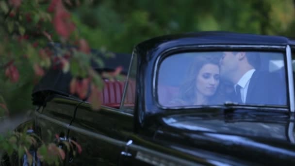 Jovem casal feliz namoro em preto retro conversível carro do vintage, homem bonito beija suavemente menina encantadora — Vídeo de Stock