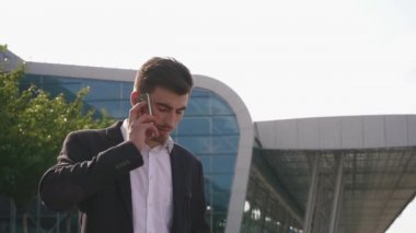 Kendine güvenen çekici sakallı işadamı telefonla konuşuyor ve iş anlaşmalarını çözüyor. Cam havaalanı duvar arka planı