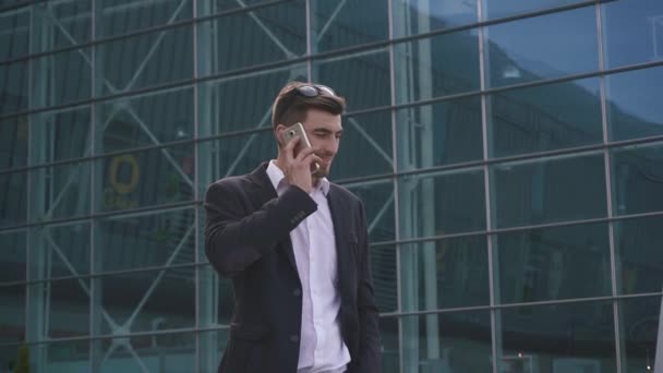 Confident young handsome bearded businessman talks by phone on the glass airport wall background — Stock Video