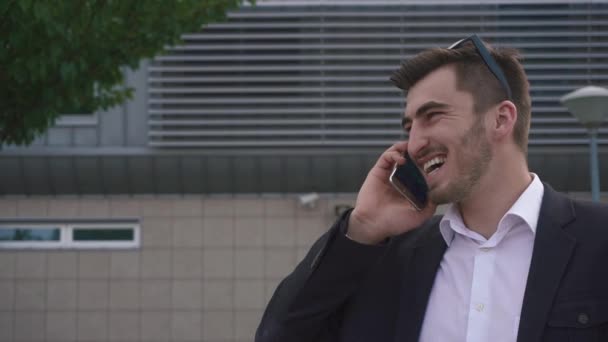 Primer plano de elegante hombre de negocios barbudo en esmoquin hablando con confianza por teléfono y sonriendo en el fondo de la pared del aeropuerto texturizado — Vídeos de Stock