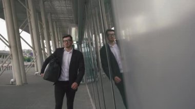 Young confident businessman with suitcase in modern airport terminal. Travelling hipster guy concept