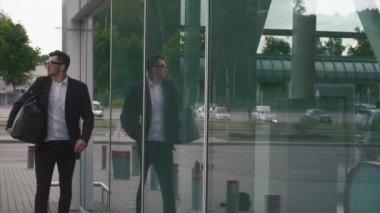 Modern havaalanı terminalinde cam arka planında bavulu olan kendine güvenen genç bir iş adamı. Gezgin hippi adam konsepti
