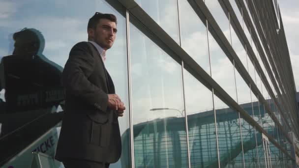 Primer plano del hombre de negocios guapo y confiado en gafas esperando su vuelo. Fondo de pared del aeropuerto de vidrio — Vídeo de stock