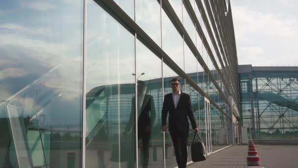 Atraktivní mladý vousatý obchodník v brýlích jde k nástupu do letadla. Pozadí skleněného letiště — Stock video
