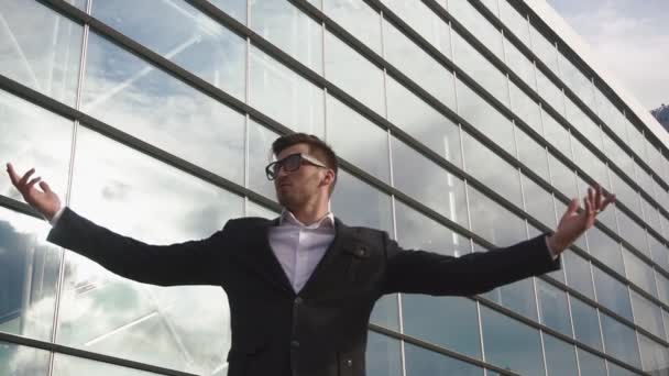Успешный молодой бизнесмен, стоящий с поднятыми руками, как победитель на стеклянном фоне — стоковое видео