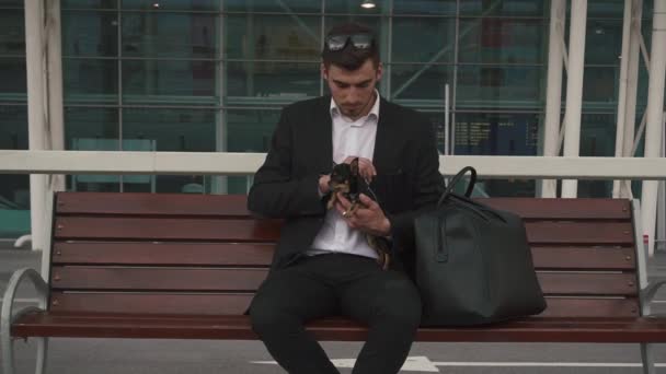 Mladý pohledný obchodník drží svého čivavského psa v náručí. Pozadí města — Stock video