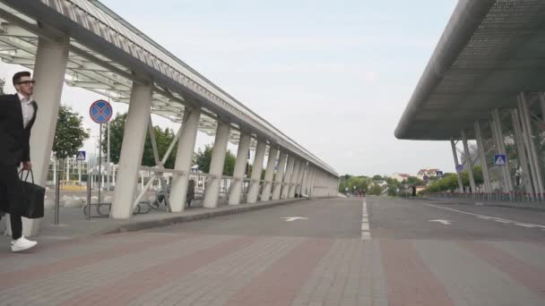 Giovane bell'uomo d'affari con la barba che corre verso il suo aereo con una grande valigia al rallentatore. Sfondo urbano della città — Video Stock