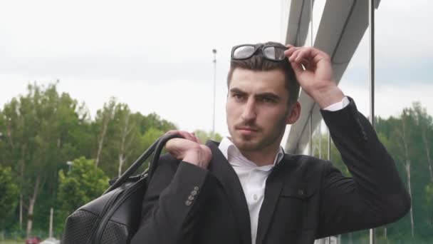 Großaufnahme des selbstbewussten gutaussehenden eleganten Geschäftsmannes, der mit einer Brille in die Kamera starrt. Flughafen-Hintergrund, Geschäftskonzept — Stockvideo