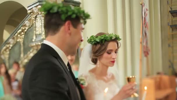 Newlyweds wearing green laurel wreathes in the church during wedding ceremony. Bride drinks wine from chalice