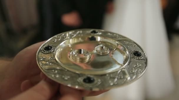 Close up of two wedding rings on gold plate holded by mans hands in the church during the ceremony — Stock Video