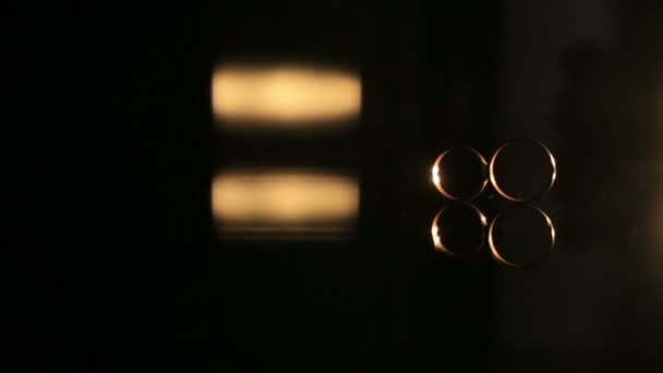 Dois anéis de casamento dourados na superfície de espelhamento, com fundo escuro iluminado por ligar e desligar a lâmpada com luz quente — Vídeo de Stock