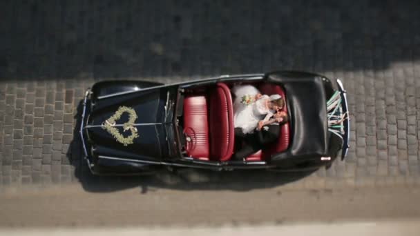 Encantadora pareja recién casada besándose apasionadamente en el asiento trasero de un coche retro en una carretera de la ciudad. Vista superior — Vídeo de stock