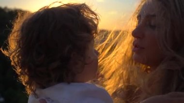 Genç Beyaz anne açık havada bebek o saçları karşı günbatımı, yakın çekim, çalış tutarken