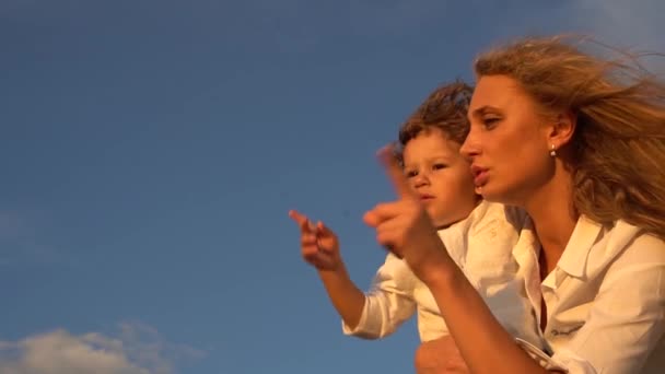 Gelukkig moeder en zoon gebaren, tonen met vinger aan te wijzen en te zwaaien over de blauwe hemelachtergrond — Stockvideo