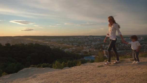 Liten pojke och hans mor kör natur vid solnedgången. De håller händerna och skrattar — Stockvideo