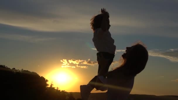 Silhouette einer Mutter mit ihrem Kleinkind gegen den Sonnenuntergang im Gegenlicht — Stockvideo