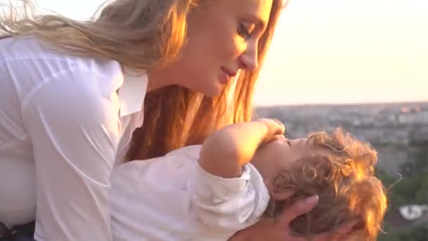 Close-up of happy blonde mother holds on hands her curly son and kissing him — Stock Video