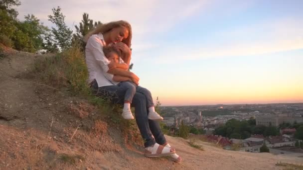 Mãe carinhosa está acariciando seu filho pequeno encaracolado bonito. Eles descansam ao ar livre ao pôr do sol — Vídeo de Stock