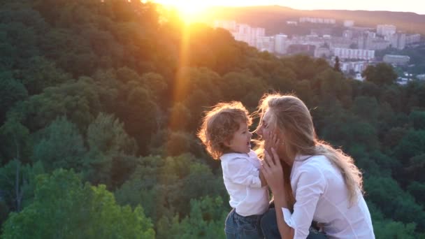 Süße lockige kleine Junge spielt mit seiner charmanten Mutter, zärtlich berühren ihre Wangen. Außenporträt — Stockvideo