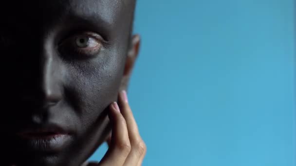 Detalle de una hermosa media cara de mujer con maquillaje negro sobre fondo azul — Vídeo de stock