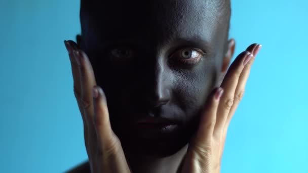 Moda, bellezza, trucco, body art. Ritratto di donna con vernice nera sulla pelle e le mani vicino al viso, primo piano, sfondo blu studio — Video Stock