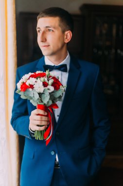 Elgant damat mavi takım elbiseli papyonlu geliniyle buluşmak için bir buket tutan bir buket tutuyor