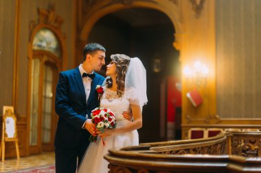 Doğal sarı ışıklar ile parlayan lüks iç arka plan ile eski ahşap korkuluk yakınında Büyüleyici gelin ve yakışıklı zarif damat