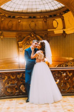 Büyüleyici gelin ve lüks iç arka plan ile eski Ahşap korkuluk çubuğu yakınındaki zarif yakışıklı damat