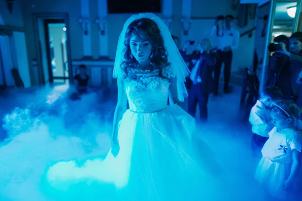 Krásná nevěsta stojí uprostřed potemnělé taneční síně v mlze. — Stock fotografie