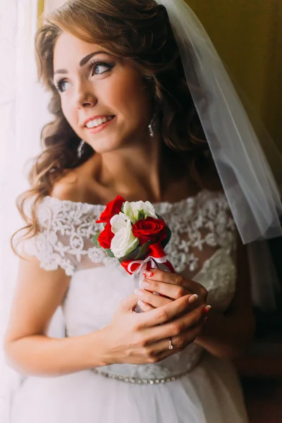 Potret close-up dari pengantin wanita yang cantik dengan gaun pengantin memegang buket lucu dengan mawar merah dan putih memimpikan masa depannya — Stok Foto