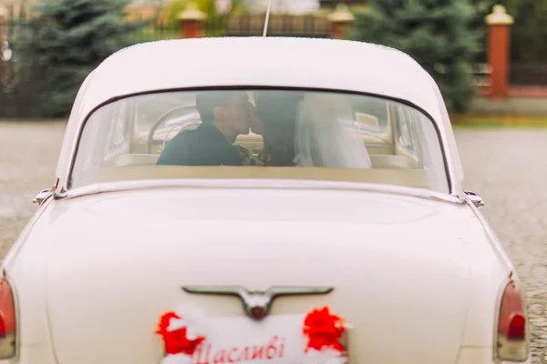 Gelukkig Newlywed paar zoenen op een achterbank van retro auto, achteraanzicht — Stockfoto