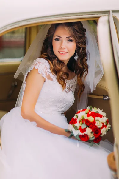 Feliz novia recién casada está sentado en un asiento trasero de coche vintage — Foto de Stock