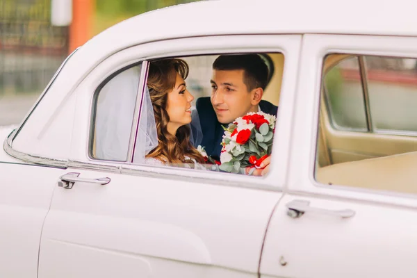 Heureux couple de jeunes mariés est assis sur un siège arrière de voiture vintage — Photo